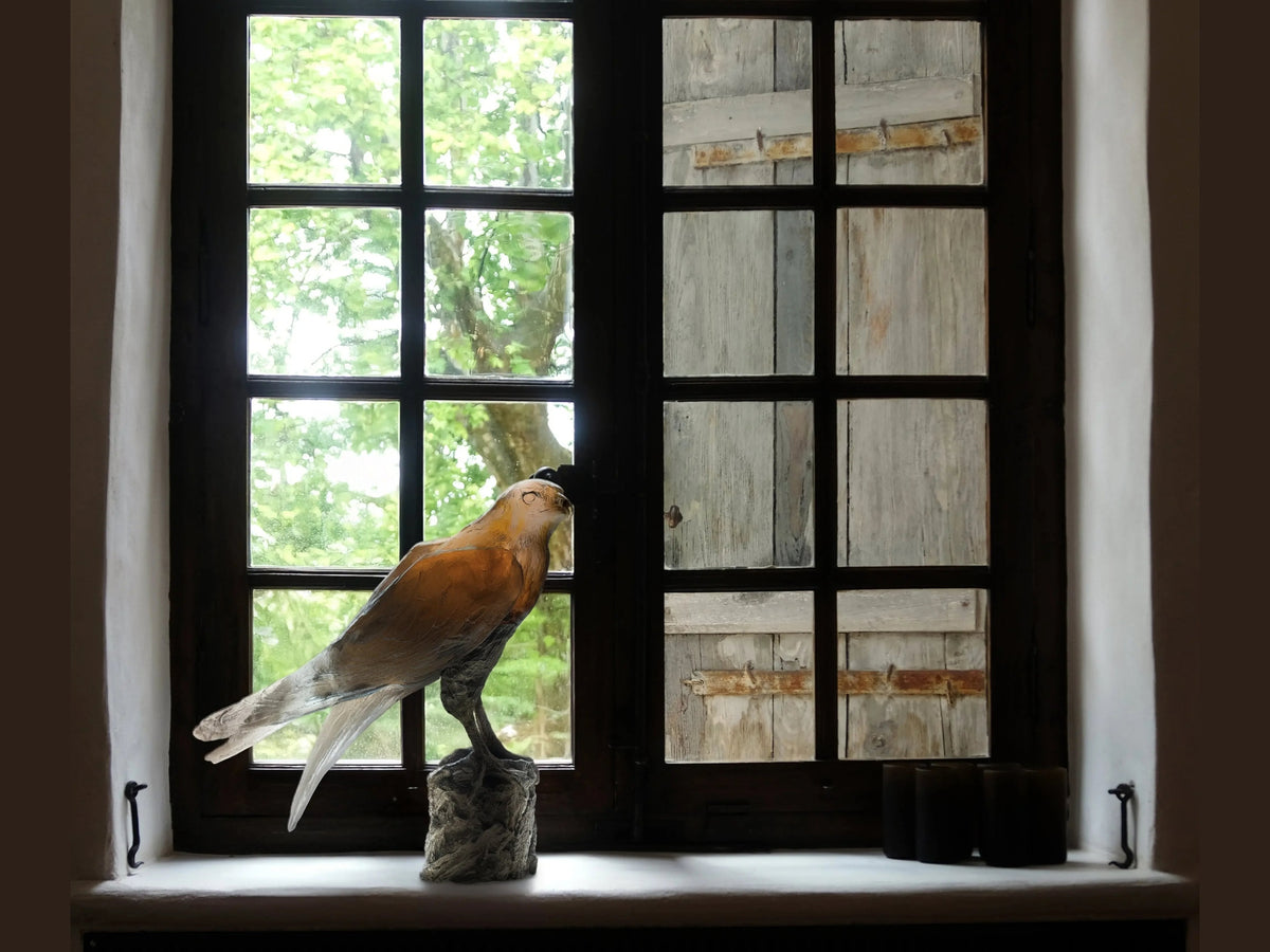 Daum Faucon Saker sculpture by Madeleine Van der Knoop on a windowsill by a window.