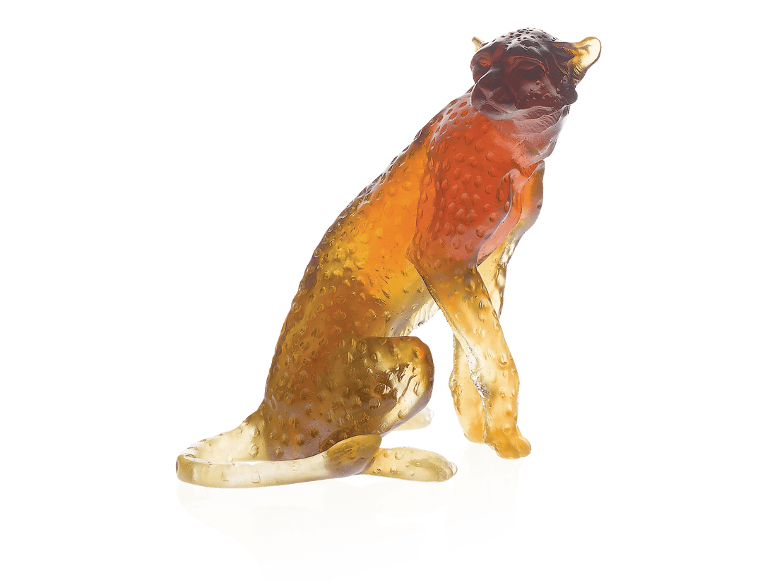 Amber-colored glass cheetah sculpture by Daum, sitting on a reflective surface.