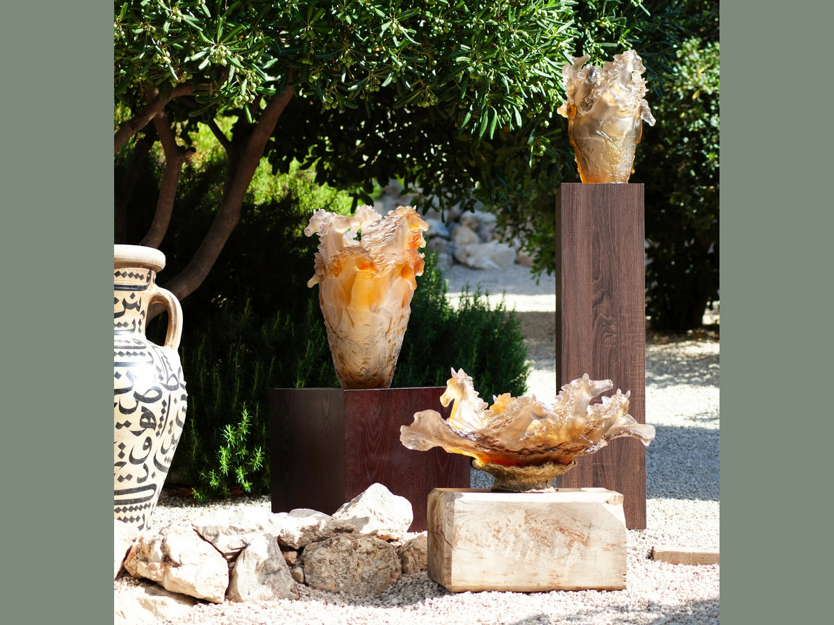 Three Daum Cavalcade centerpieces in iced brown glass displayed outdoors on plinths.