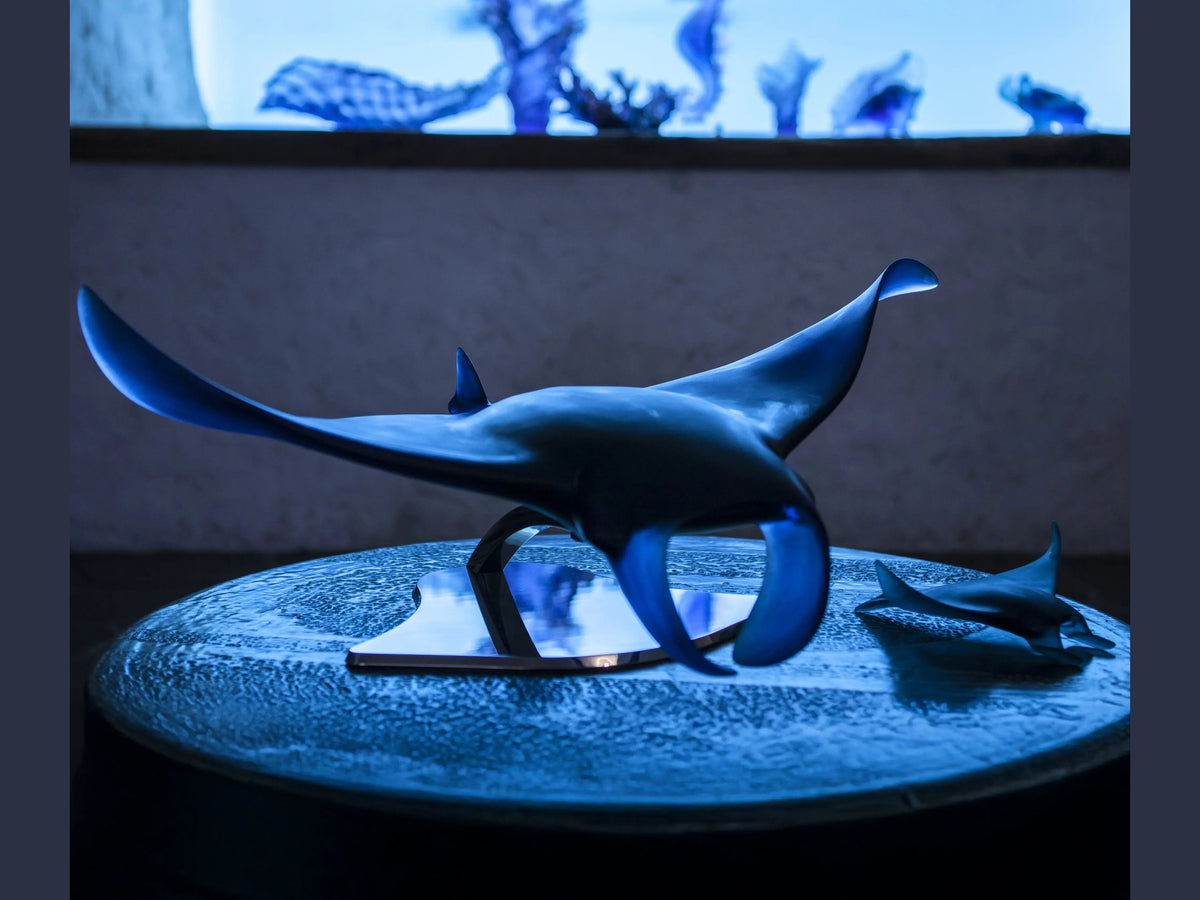 Blue Daum manta ray glass sculpture by Umberto Nuzzo on a textured table.