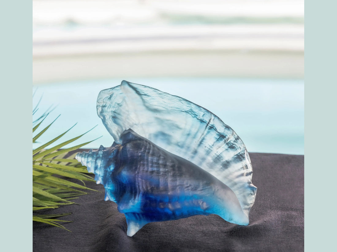 Daum Mer de Corail blue glass conch shell sculpture on a green background